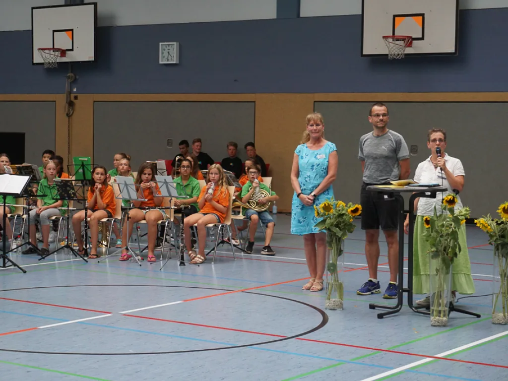 Drei Personen stehen am Rednerpult in der Halle.